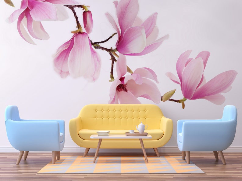 May include: A living room interior design with a yellow sofa, two light blue armchairs, and a coffee table. The wall features a floral wallpaper with pink magnolia blossoms.