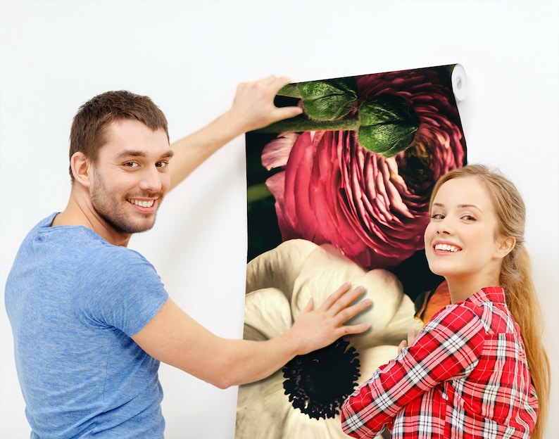 May include: A couple are hanging up a floral wallpaper with large pink and white flowers. The wallpaper has a dark background and the flowers are in focus.