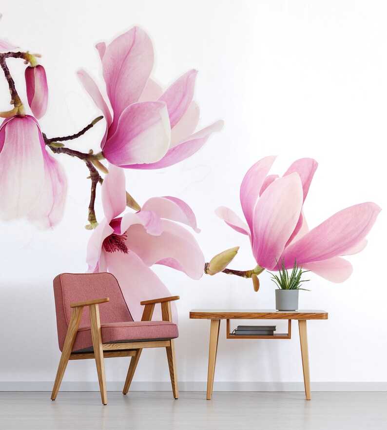 May include: A pink magnolia flower wallpaper mural with a pink armchair and a wooden table with a potted plant on top.