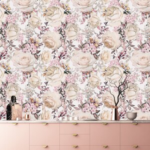 K&ouml;nnte beinhalten: Ein rosa K&uuml;chenschrank mit goldenen Griffen vor einem wei&szlig;en Hintergrund mit einem floralen Tapetenmuster mit wei&szlig;en Rosen und rosa Bl&uuml;ten.