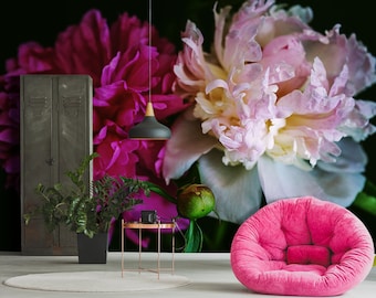 May include: A pink and white peony flower with a dark background. A black pendant light hangs above a small table with a plant and a camera on it. A pink armchair sits in front of the table.