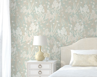 May include: A white bed with a white duvet cover and a beige headboard. The bed is in a room with a light blue floral wallpaper, a white nightstand with three drawers, and a white lamp with a beige shade.