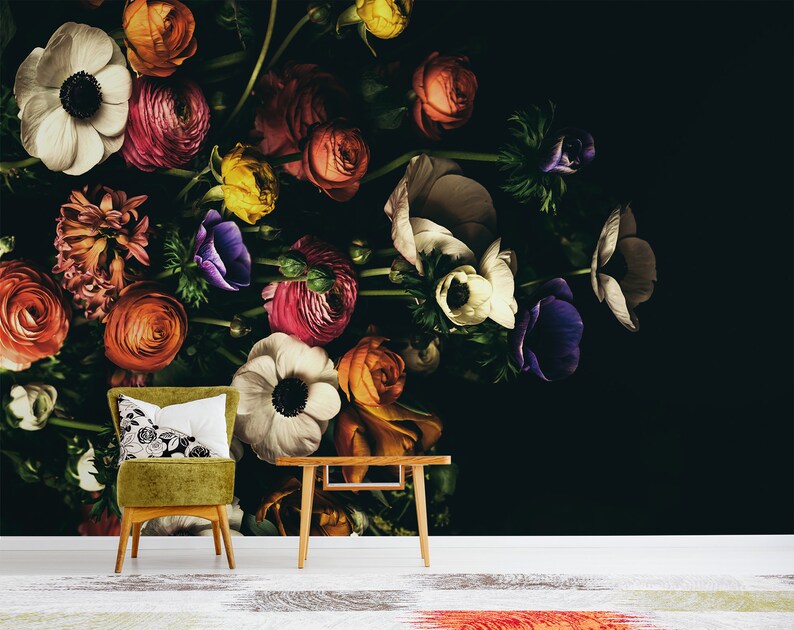 May include: A dark background with a large bouquet of colourful flowers, including white, pink, red, orange, yellow, purple, and green. The flowers are arranged in a vase and are spilling over the edge. A green chair with a white cushion is in the foreground.