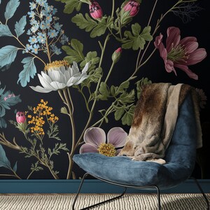 May include: A blue velvet armchair with a brown faux fur throw sits in front of a black wall with a floral wallpaper featuring pink, white, and yellow flowers.