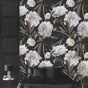 May include: A black and white floral wallpaper featuring large white peonies with green leaves and stems. The wallpaper is displayed on a wall behind a black bed with black bedding and pillows.
