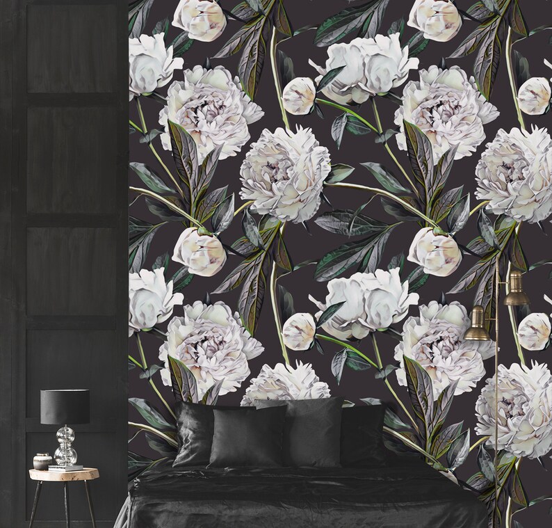 May include: A black and white floral wallpaper featuring large white peonies with green leaves and stems. The wallpaper is displayed on a wall behind a black bed with black bedding and pillows.