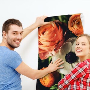 May include: A couple is hanging up a floral wallpaper with large orange and white flowers. The wallpaper has a vintage feel.
