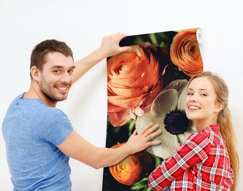 May include: A couple is hanging up a floral wallpaper with large orange and white flowers. The wallpaper has a vintage feel.