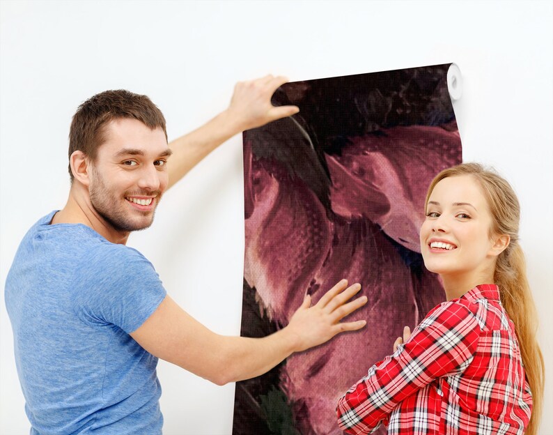 May include: A couple is hanging up a large abstract floral wallpaper with a dark background and pink and purple hues. The wallpaper is being applied to a white wall.
