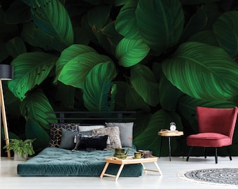 May include: A green tropical leaf wallpaper mural with a dark green background. The mural is in a living room setting with a green futon, a red chair, and a wooden side table.