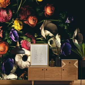 May include: A dark wood cabinet with two drawers and two doors, featuring a floral wallpaper with a variety of colourful flowers, including red, yellow, purple, and white. A gold framed picture hangs above the cabinet, and a gold leaf plant sits on the cabinet.