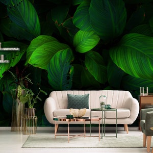 K&ouml;nnte beinhalten: Ein Wohnzimmer-Interieur mit einem wei&szlig;en Sofa und zwei Couchtischen. Die Wand hinter dem Sofa ist mit einer gr&uuml;nen tropischen Bl&auml;ttertapete bedeckt.