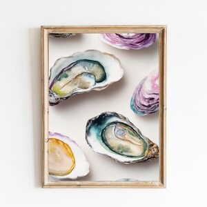 May include: A framed watercolour painting featuring open oyster shells. The shells are depicted in shades of blue, green, purple, and yellow against a white backdrop. The frame is gold-coloured. A still life artwork.