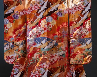 May include: A vibrant orange kimono with a repeating pattern of white cranes, flowers, and landscapes. The traditional Japanese garment features red, gold, and blue accents. The kimono is displayed against a dark background.