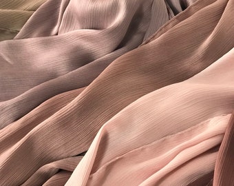 May include: A collection of soft, sheer fabric in various shades of brown, pink, and beige. The fabric is arranged in a layered, flowing pattern, creating a sense of depth and texture.