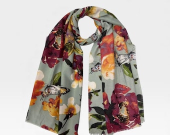 May include: A light green scarf with a floral and butterfly pattern. The scarf features large burgundy, orange, and yellow flowers, along with white butterflies. The scarf is made of a soft material and has a fringed edge.