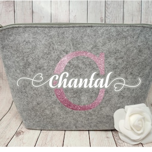 Könnte beinhalten: Graue Filztasche mit Reißverschluss, einem pinkfarbenen Glitzerbuchstaben C und dem Namen Chantal in weißer Kursivschrift.