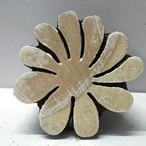 Könnte beinhalten: Ein Holzblock-Stempel mit einem geschnitzten Design einer Blume mit 12 Blütenblättern. Der Stempel ist aus hellem braunem Holz gefertigt und hat eine weiß getünchte Oberfläche.