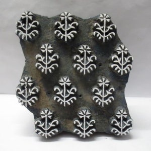 Könnte beinhalten: Ein dunkelgrauer Holzblock-Stempel mit einem sich wiederholenden Muster aus weißen, stilisierten floralen Designs.
