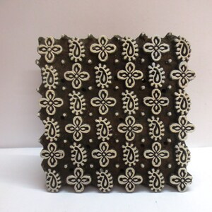 Könnte beinhalten: Ein Holz-Druckblock mit einem sich wiederholenden Muster aus Paisley- und Blumenmotiven. Der Block ist braun mit weißen Designs.