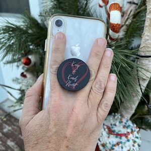 May include: A black phone pop socket with a red heart and the text "Keep a Kind Heart" in white lettering.