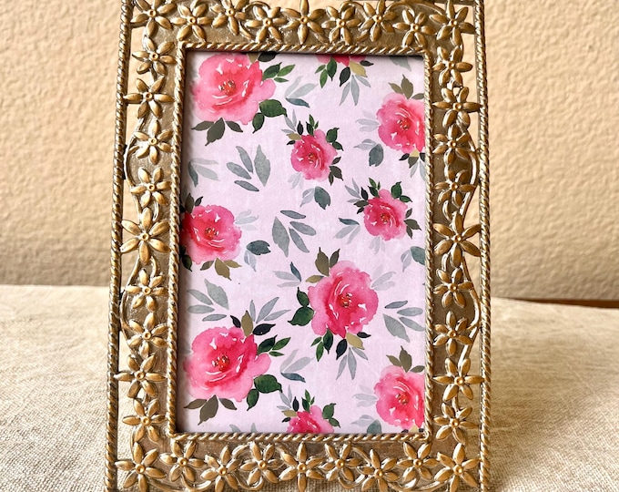 Vintage frame holds a 3 1/2 x 5  1/2 inch image gold and silver with ornate floral details.