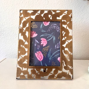 May include: A gold metal picture frame with a cut-out design of leaves and flowers. The frame is empty and ready to hold a photo.