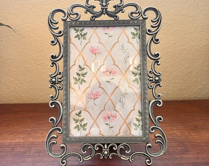 Vintage 8 1/2"x6 silver metal frame with ornate detailed border holds a 3 1/2"x5 1/2" image. Stand only
