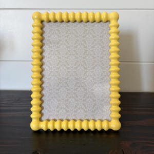 May include: A rectangular picture frame with a bright yellow, beaded, or bobbin-style border. The frame surrounds a central insert featuring a light beige background with a repeating white damask pattern. The frame has a smooth, matte finish.
