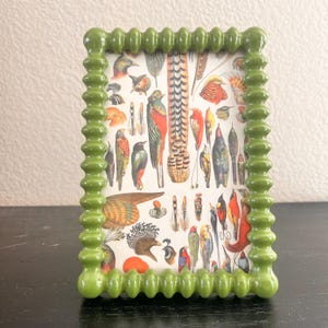 In einem grün emaillierten Noppenrahmen im Vintage-Stil befindet sich ein 9,5 x 13,5 cm großes Bild. 11 x 15 cm