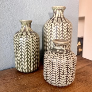 May include: Three ceramic vases with a brown and white herringbone pattern. The vases are different sizes and are arranged in a row on a wooden surface.
