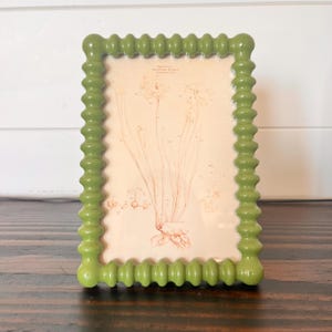 In einem grün emaillierten Noppenrahmen im Vintage-Stil befindet sich ein 9,5 x 13,5 cm großes Bild. 11 x 15 cm