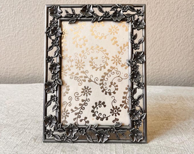 Vintage 5 1/2 x7 1/2 inch silver frame with floral detail and hand made paper holds a 4x 6 inch image.