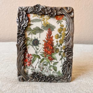 Vintage Art Deco style 5 1/2 x4 inch silver frame with floral detail around window holds a 3 x 4 1/4 &quot; image