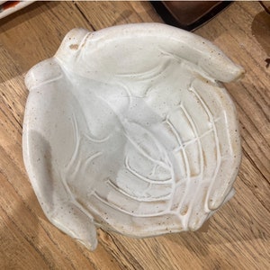 Peut inclure: Un bol en céramique blanche en forme de deux mains jointes. Le bol a une surface texturée et est parfait pour contenir de petits objets.