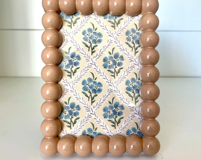 Vintage style tan colored 7”x 5” hob knob frame holds a 3 1/2”x 5 1/4” photo