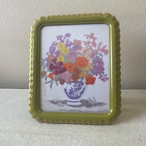 May include: A framed floral print featuring a colorful bouquet in a blue and white vase. The frame is a light green with a scalloped edge and gold trim. The flowers include orange, purple, yellow, and red blooms.