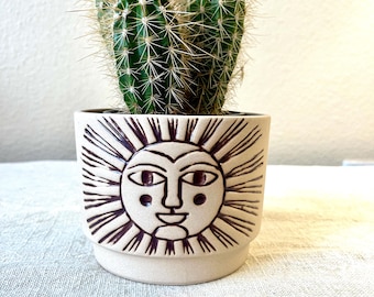 Beige colored ceramic planter with embossed sun face distressed rust color hold the 4 inch pot.