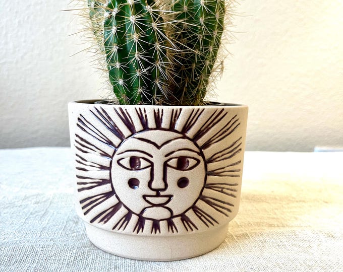 Beige colored ceramic planter with embossed sun face distressed rust color hold the 4 inch pot.