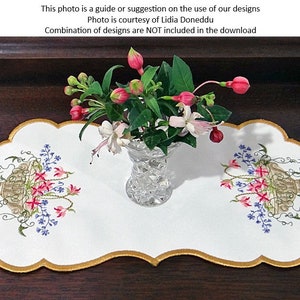 May include: White embroidered table runner with a scalloped edge and gold trim. The runner features two embroidered floral designs with a vase of pink and white flowers in the center.