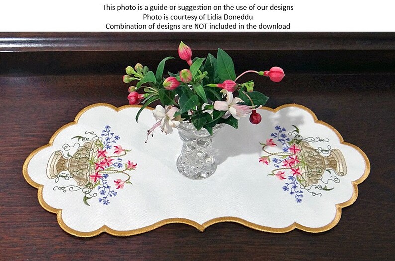 May include: White embroidered table runner with a scalloped edge and gold trim. The runner features two embroidered floral designs with a vase of pink and white flowers in the center.