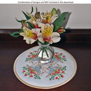 May include: A white embroidered round table runner with a gold trim and a floral design. A vase with a bouquet of yellow and white flowers sits on top of the runner.