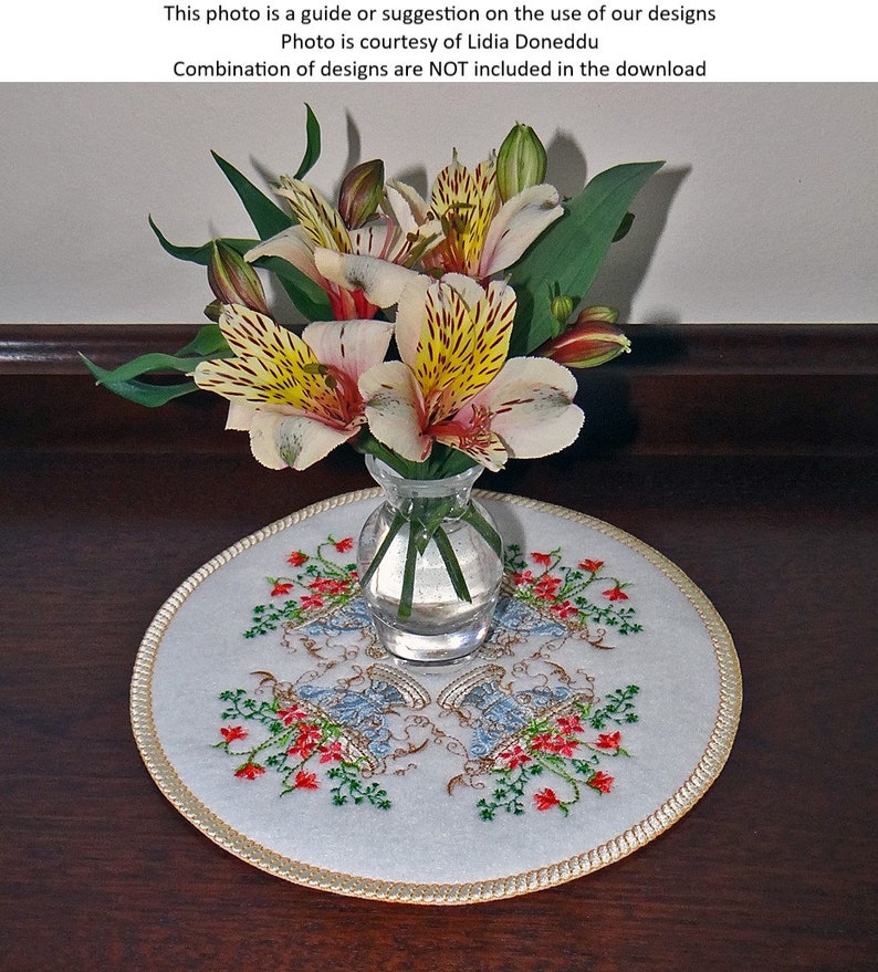 May include: A white embroidered round table runner with a gold trim and a floral design. A vase with a bouquet of yellow and white flowers sits on top of the runner.