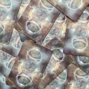 Op de afbeelding: Een stapel tarotkaarten met een mystiek ontwerp met meerdere overlappende cirkels met een maan- en sterrenpatroon in grijstinten, wit en blauw.