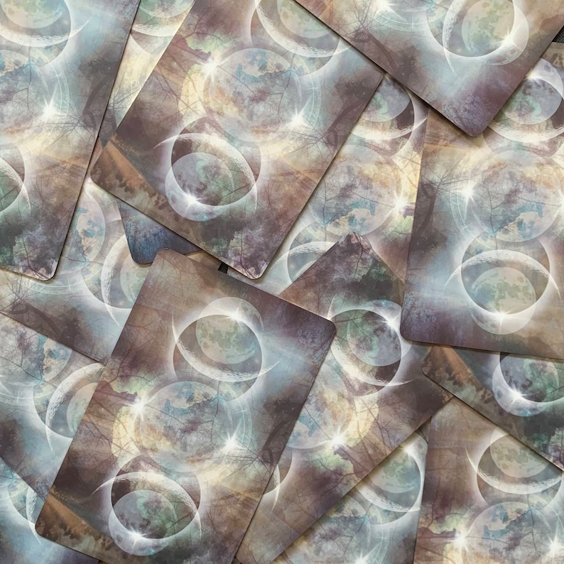 Op de afbeelding: Een stapel tarotkaarten met een mystiek ontwerp met meerdere overlappende cirkels met een maan- en sterrenpatroon in grijstinten, wit en blauw.