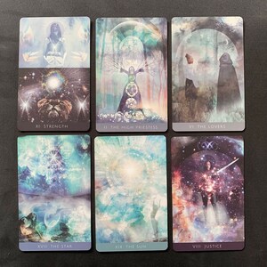 Op de afbeelding: Een set van negen tarotkaarten met kleurrijke, abstracte ontwerpen. De kaarten tonen afbeeldingen van een vrouw met een kroon, een vrouw met een zwaard, een vrouw met een leeuw, een vrouw met een ster, een vrouw met een zon en een vrouw met een weegschaal. De kaarten zijn gelabeld met de namen van de tarotkaarten: Kracht, Hogepriesteres, Geliefden, Ster, Zon en Rechtvaardigheid.