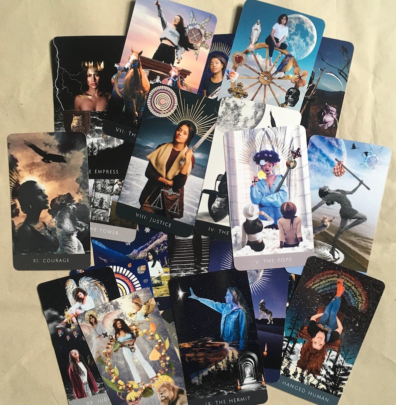 May include: A spread of tarot cards featuring colorful illustrations and text. The cards include "XI: Courage", "VII: The Empress", "VIII: Justice", "IV: The", "The Tower", "V: The Pope", "JUD", "IX: The Hermit", and "Hanged Human".