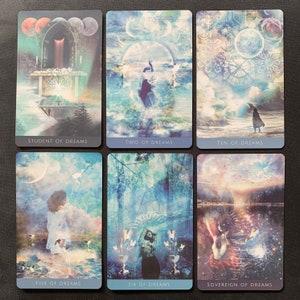 Op de afbeelding: Een set van tien tarotkaarten uit het Dreams Tarot deck. De kaarten hebben een blauw en wit kleurenschema met afbeeldingen van mensen, landschappen en hemellichamen. De kaarttitels zijn "Student of Dreams", "Two of Dreams", "Ten of Dreams", "Five of Dreams", "Six of Dreams" en "Sovereign of Dreams".