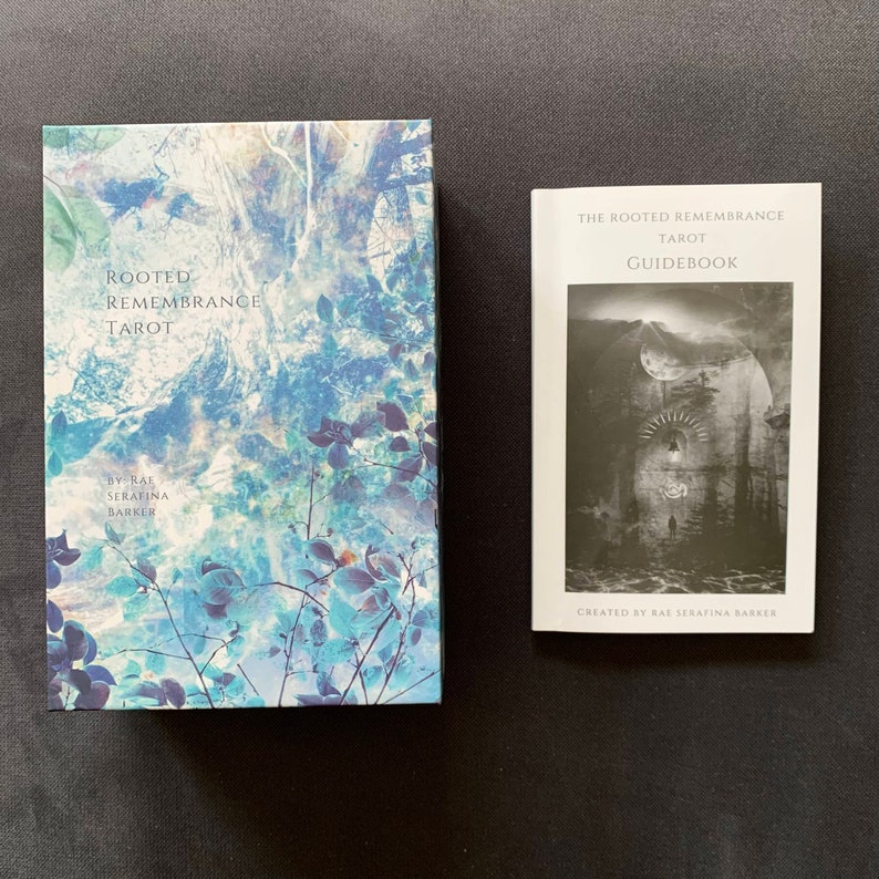 Op de afbeelding: Een doos en een handleiding voor het Rooted Remembrance Tarot-deck. De doos heeft een blauwe en witte aquarelachtige afbeelding van bomen en bladeren. De handleiding heeft een zwart-witte afbeelding van een gebouw met een maan en sterren aan de hemel.