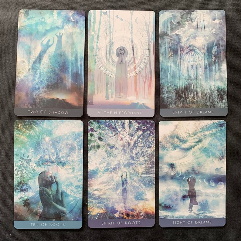 Op de afbeelding: Een set van tien tarotkaarten met blauwe en witte achtergronden. De kaarten tonen afbeeldingen van een schaduwfiguur, een vrouw in een witte robe, een gebouw met een groot raam, een vrouw met haar handen gevouwen, een boom met een helder licht en een vrouw die in een bewolkte lucht staat. De kaarten zijn gelabeld met de namen van de kaarten: Twee van Schaduw, V: De Hi&euml;rofant, Geest van Dromen, Tien van Wortels, Geest van Wortels en Acht van Dromen.